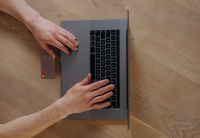 person typing on a laptop with a credit card next to them